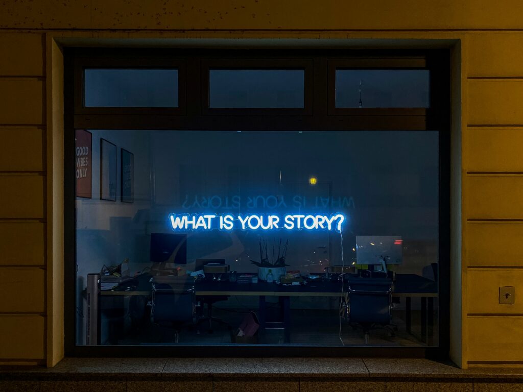 An image of a window with the words "WHAT IS YOUR STORY?" written in Neon