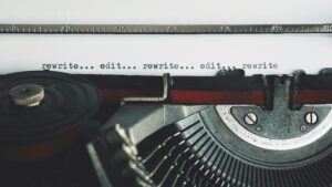 A close-up of a red typewriter with the words "rewrite... edit... rewrite... edit... rewrite" typed onto a sheet of paper
